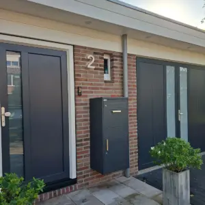 Pakketbrievenbus antraciet aan een bakstenen gevel naast de voordeur